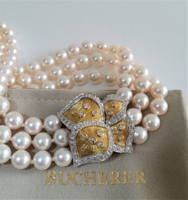 Bucherer Triple Row Akoya Pearl Necklace, on 18ct gold clasp designed as four stylised petals edged with 1.22cts small diamonds, with original receipt, Bucherer box and pouch